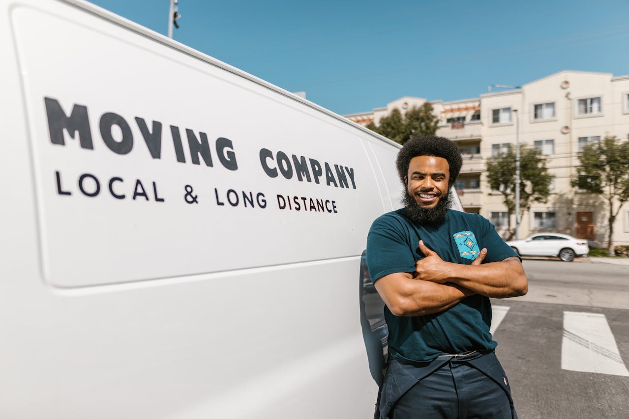 A man in black pants and shirt leaning on a van with his hands crossed.