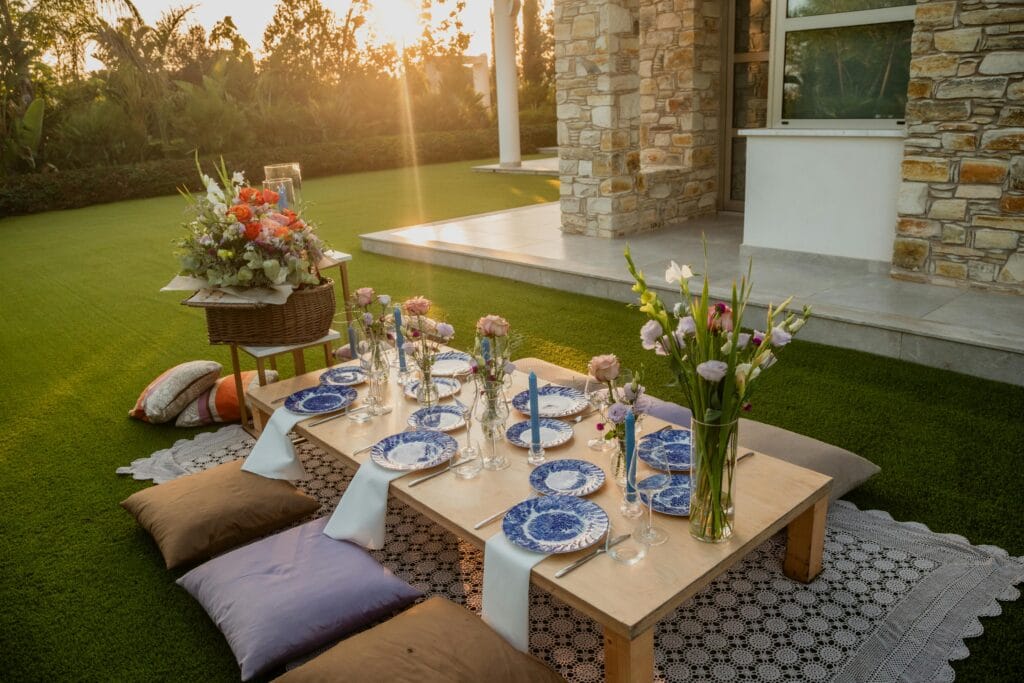 Outdoor summer dining setup on a lawn near a stone house.